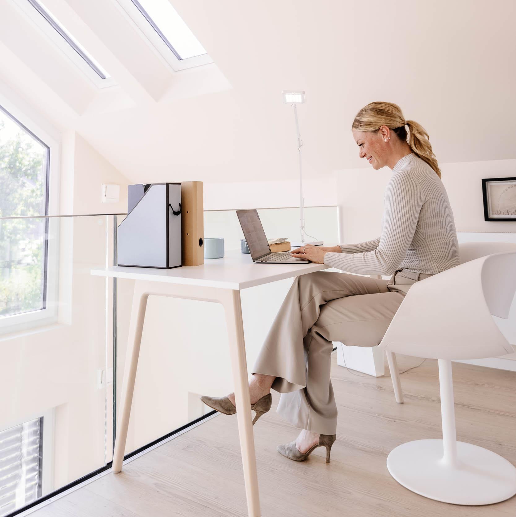 Eine Frau sitzt am Schreibtisch und arbeitet am Laptop.