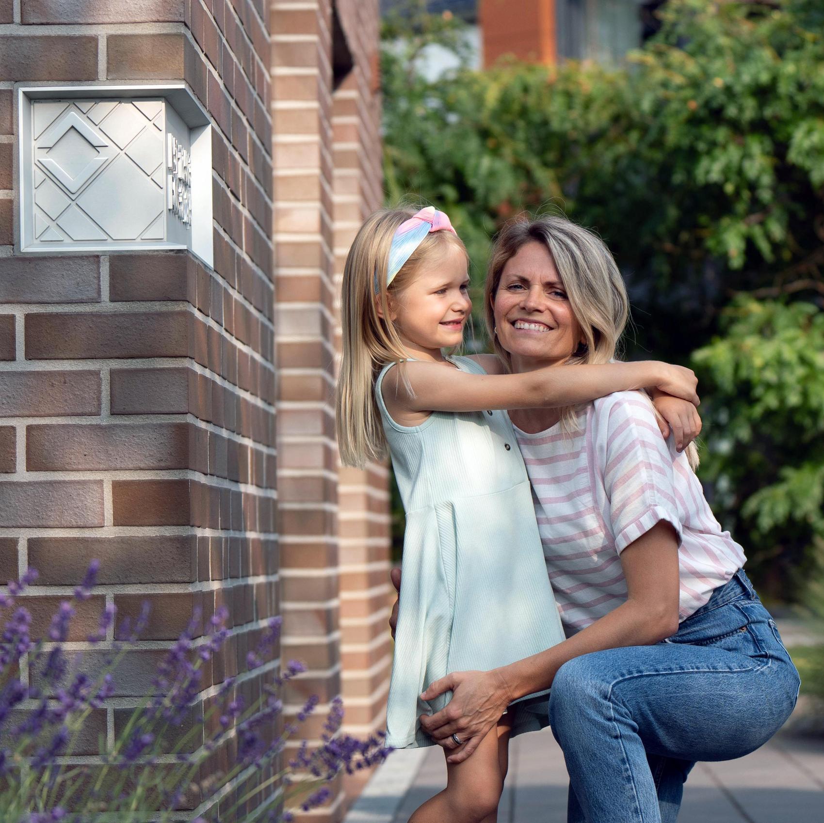 Mutter und Tochter umarmen sich neben dem Viebrockhaus-Eckstein in der Hausecke.