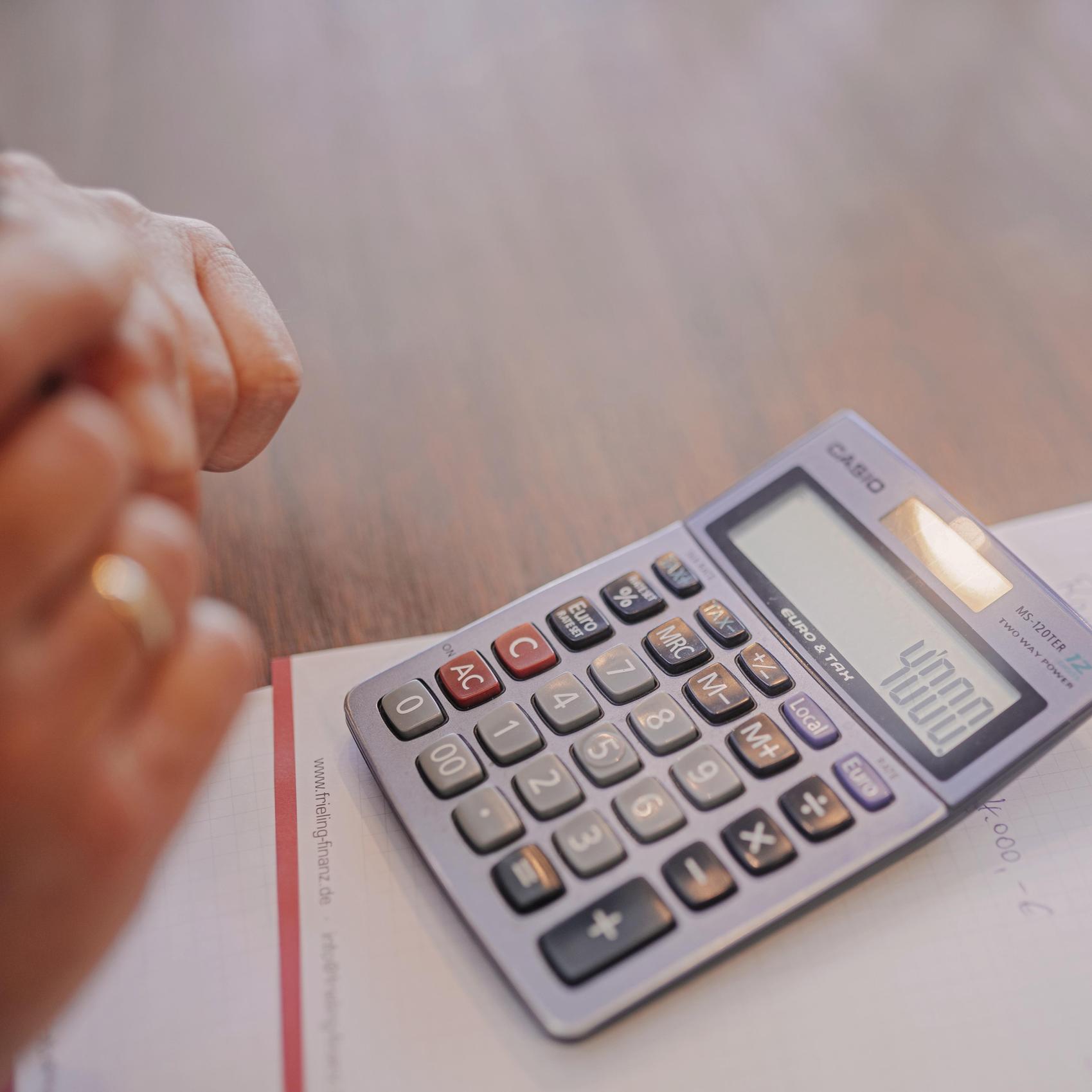 Ein Taschenrechner liegt auf einem Schreibblock, daneben sind zwei Hände zu sehen