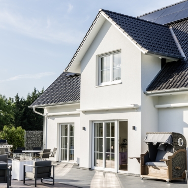 Ein weißes Haus, vom Garten ausgesehen, hat Photovoltaikanlagen installiert.